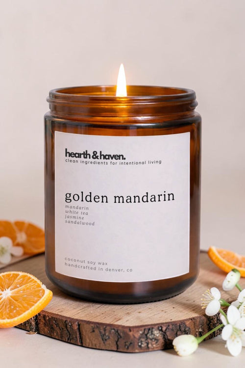 hearth & haven Golden Mandarin candle burning in amber glass jar surrounded by fresh mandarin slices, phthalate-free mandarin white tea jasmine and sandalwood fragrance blend, handcrafted in Denver CO